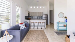 A compact living space with a kitchenette, a sofa with a patterned pillow, a small bar area, and a decorative mirror. - Aguada Ocean Club 3A - 2 Bed 1 Bath Suite (Aguada)