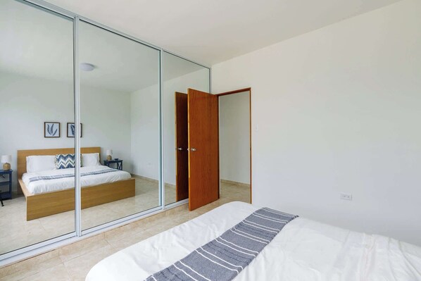 A bedroom with a bed, a nightstand, a bedside table, a wooden door, and a glass partition.
