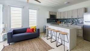 Eine moderne Küche mit einer zentralen Kochinsel, Barhocker und einem dunkelblauen Sofa mit roten und gelben Kissen.