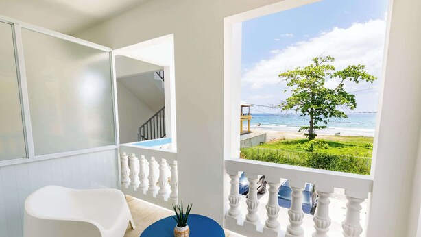 Ein Balkon mit Blick auf das Meer, ein weißer Stuhl, ein blauer Tisch und ein Blumentopf.