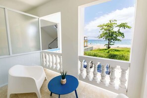 A balcony with a view of the sea, a white chair, a blue table, and a potted plant.