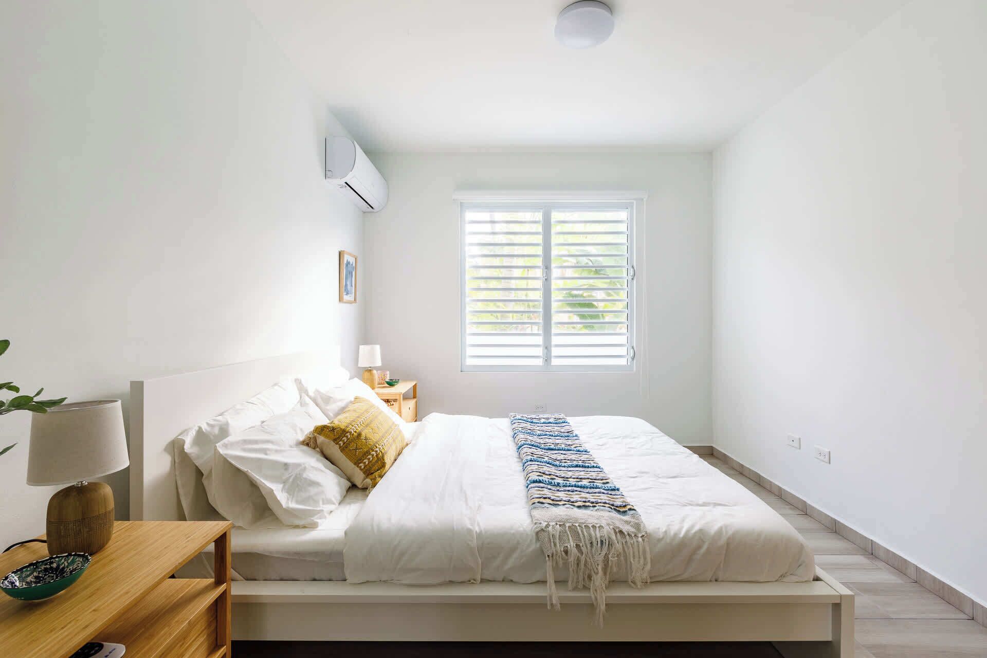 Un dormitorio con cama, mesita de noche, lámpara y ventana con persianas.