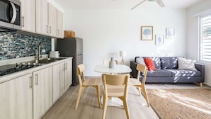Eine moderne Küche mit Mikrowelle, Herd und Kühlschrank. Ein Essbereich mit Tisch und Stühlen ist vorhanden. Ein Deckenventilator ist sichtbar, und das Zimmer hat ein Fenster mit Jalousien.
