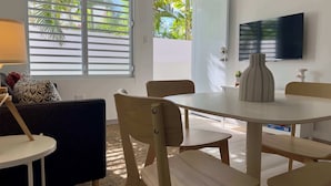 Ein modernes Wohnzimmer mit einem runden Esstisch, Holzstühlen, einer Couch und einem an der Wand montierten Fernseher.
