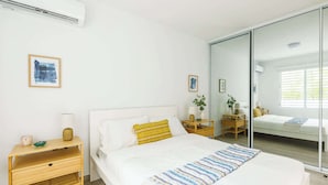 Ein modernes Schlafzimmer mit einem Bett, Nachttischen, einem Spiegel und Kunstwerken an den Wänden.