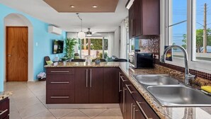 A modern kitchen with dark cabinetry, granite countertops, a large island, and a window providing a view of the outdoors. - Blue Water View | Breathtaking 2 bedroom apartment with amazing water views! (Rincon)