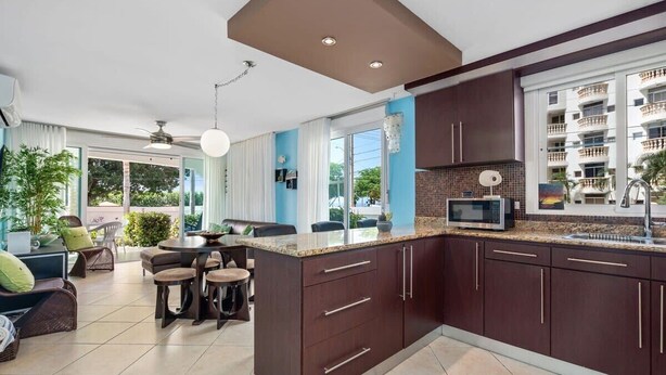 A modern kitchen with dark cabinets, a microwave, and a large window overlooking a residential area. - Blue Water View | Breathtaking 2 bedroom apartment with amazing water views! (Rincon)