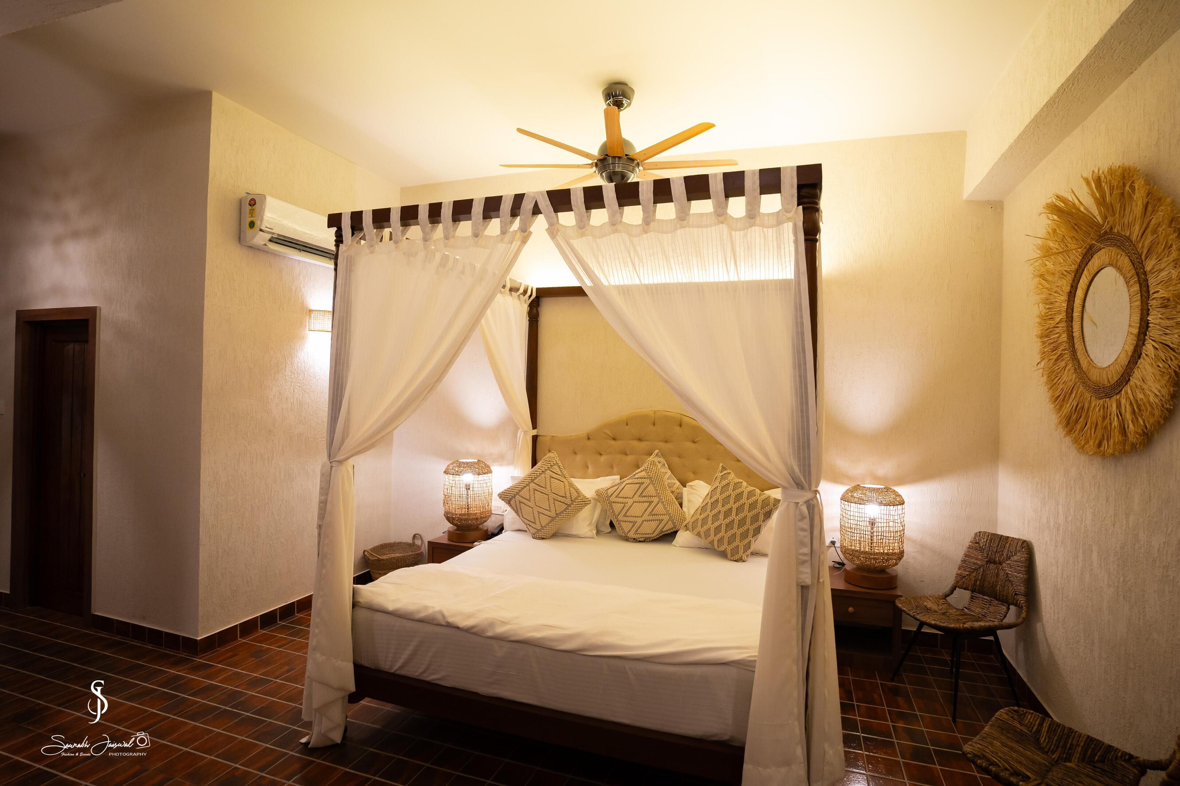 A four-poster bed with a ceiling fan, a wall-mounted air conditioner, and a decorative mirror.