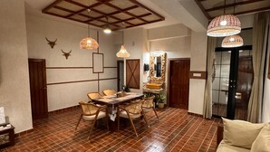 A spacious dining area with a wooden table and chairs, a round wooden stool, and two hanging wicker lamps. - Shanti Inn Dormitory (Varanasi)