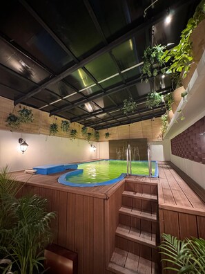 Un área de hidromasaje con cubierta de madera, escalones que conducen al jacuzzi y plantas colgantes.