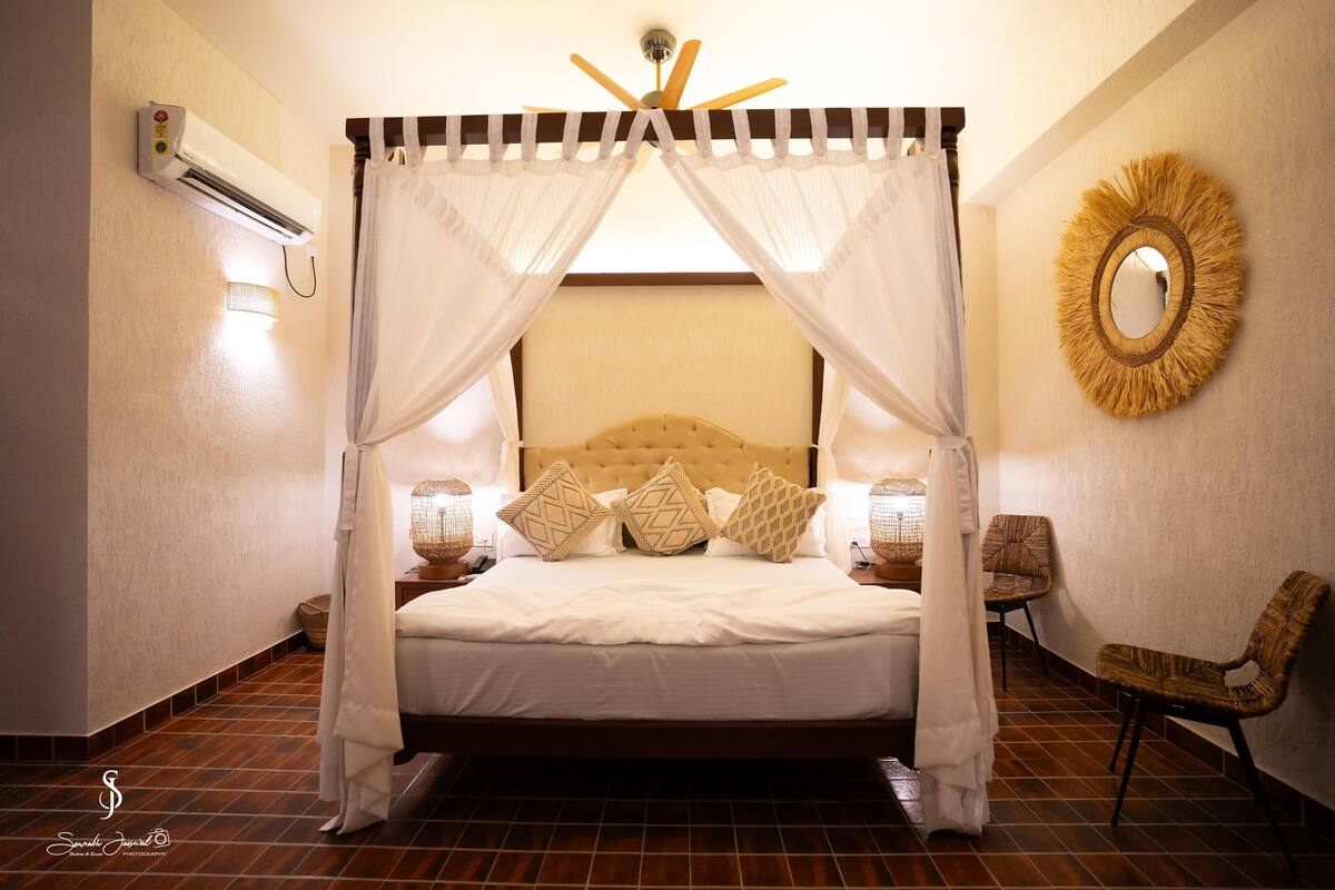 A bed with a canopy, two bedside lamps, and a round mirror on the wall.