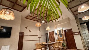 A dining area with a round table, wicker chairs, and hanging wicker lamps. - Shanti Inn Dormitory (Varanasi)