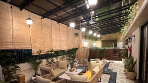An indoor patio area with wicker furniture, potted plants, and a tiled floor. - Shanti Inn Dormitory (Varanasi)
