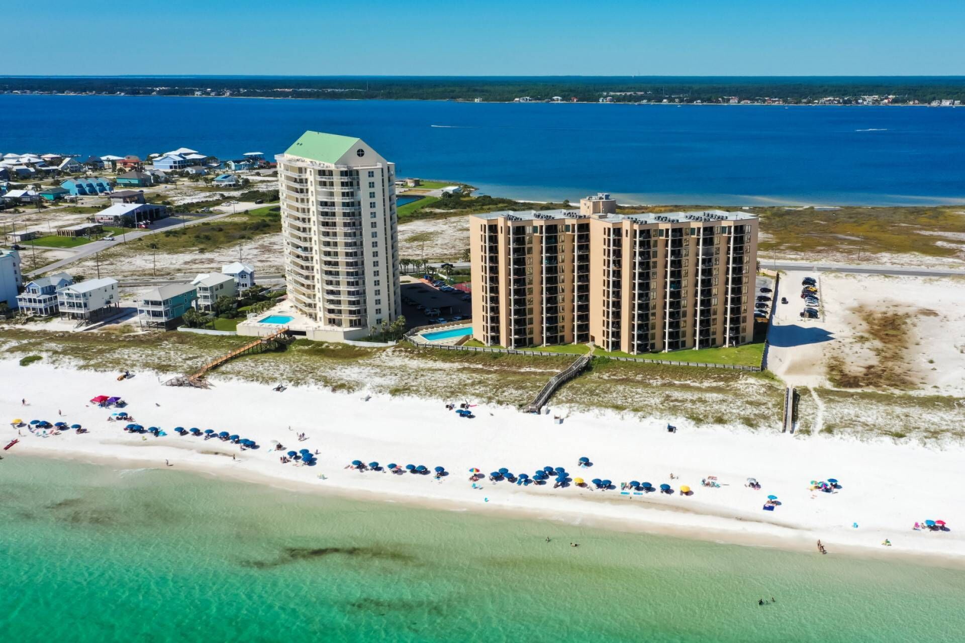 An aerial view of a coastal area with two large buildings, a beach, and a clear blue sea.