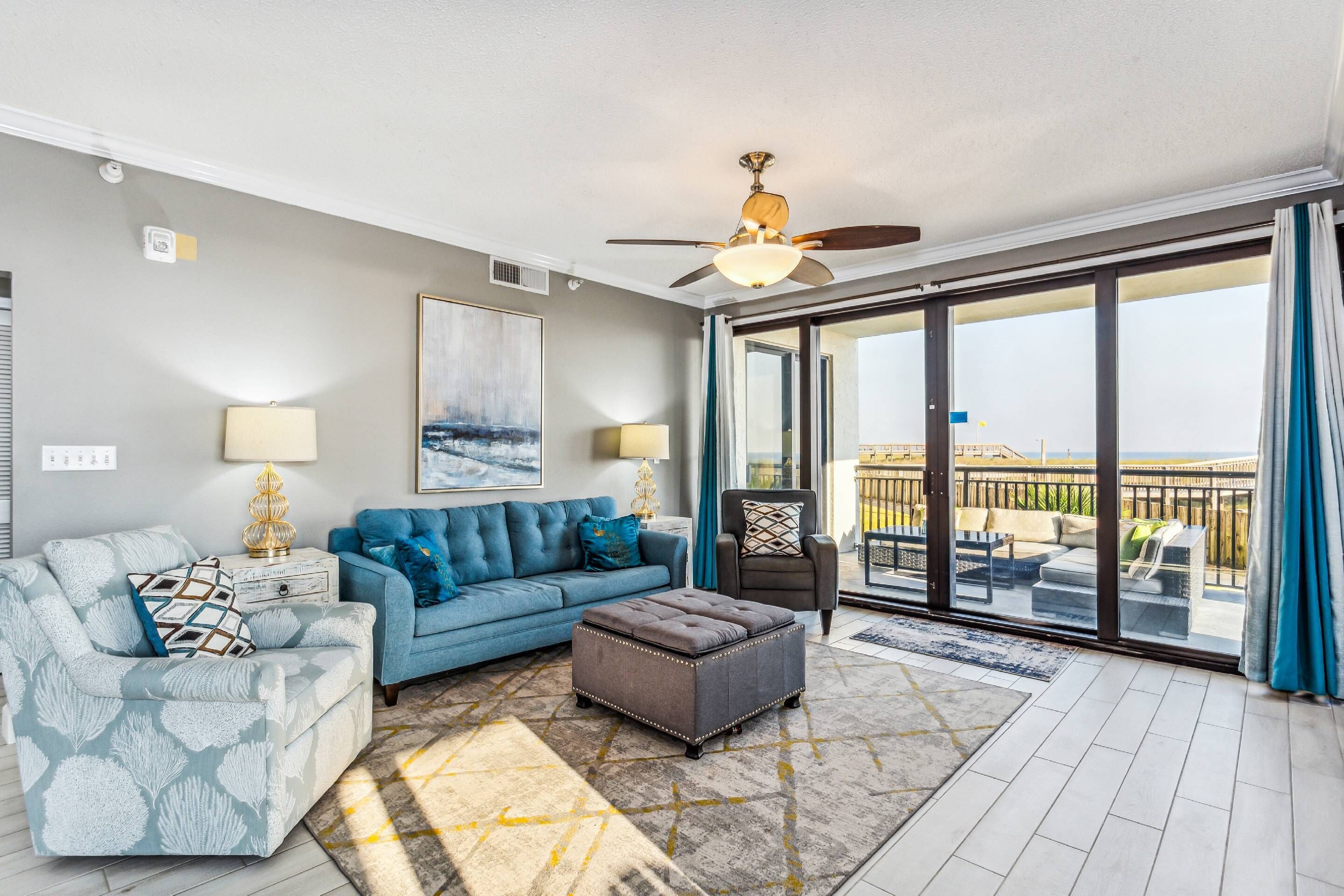 A living room with a blue sofa, a matching ottoman, and a ceiling fan.