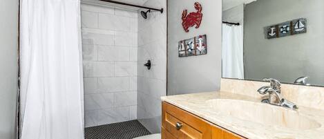 Une salle de bain avec un rideau de douche blanc, des toilettes blanches, un meuble-lavabo en bois avec un plan de travail en marbre et un miroir fixé au mur.