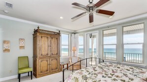A bedroom with a large bed, a wooden cabinet, a green chair, and a ceiling fan. - Luxurious Beachfront End Unit Townhome |Unobstructed Gulf Views |Step onto Sugar White Sands |Garage (Navarre Beach)
