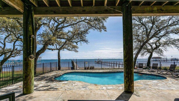 A pool area with a view of the sea, surrounded by stone tiles and wooden pergola.