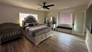 A bedroom with a bed, a crib, a ceiling fan, a window with blinds, and a door. - Modern Home w/Gameroom near Airport Beaches Disney (Long Beach)