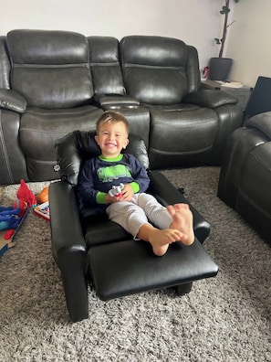 Un bambino seduto su un divano in pelle nera in un soggiorno con tappeto grigio.