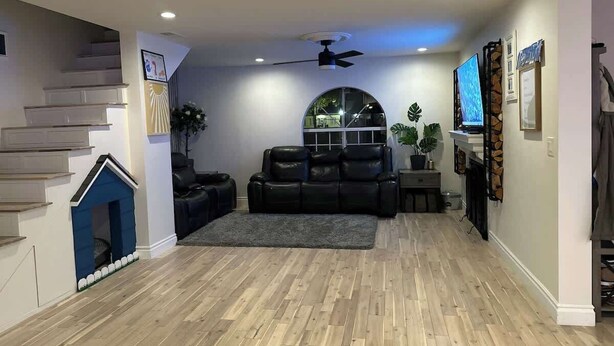 A living room with a staircase, a black leather sofa, a television, and a plant. - Modern Home w/Gameroom near Airport Beaches Disney (Long Beach)