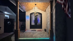 A hotel entrance with a stone wall, a wooden ceiling, and a black door with a decorative wreath. - Modern Home w/Gameroom near Airport Beaches Disney (Long Beach)