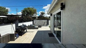A patio area with a barbecue setup, a stone wall, and a glass door leading to a covered space. - Modern Home w/Gameroom near Airport Beaches Disney (Long Beach)