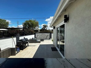 Un'area patio con un angolo barbecue, un muro in pietra e una porta in vetro che dà su uno spazio coperto.