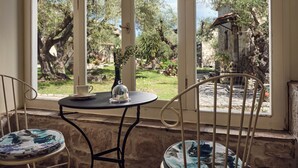 Quarto com vista para um jardim através de grandes janelas, uma mesa pequena com um vaso e duas cadeiras.