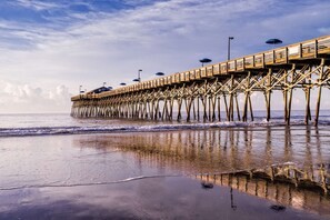 A wooden pier extending into the water with umbrellas and street lamps.