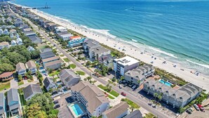An aerial view of a coastal residential area with a beachfront, including houses, a road, and a swimming pool. - *Fall into Savings-20% Off New Bookings thru 2026* (Surfside Beach)
