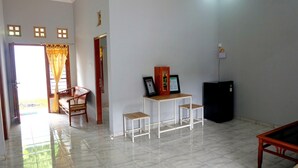 Quarto com sofá de madeira, uma pequena mesa com dois bancos, um armário com certificados emoldurados, uma geladeira preta e uma porta que dá para uma área externa.