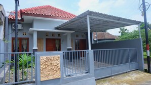 Um edifício residencial com telhado de telhas vermelhas, varanda coberta e entrada com portão.
