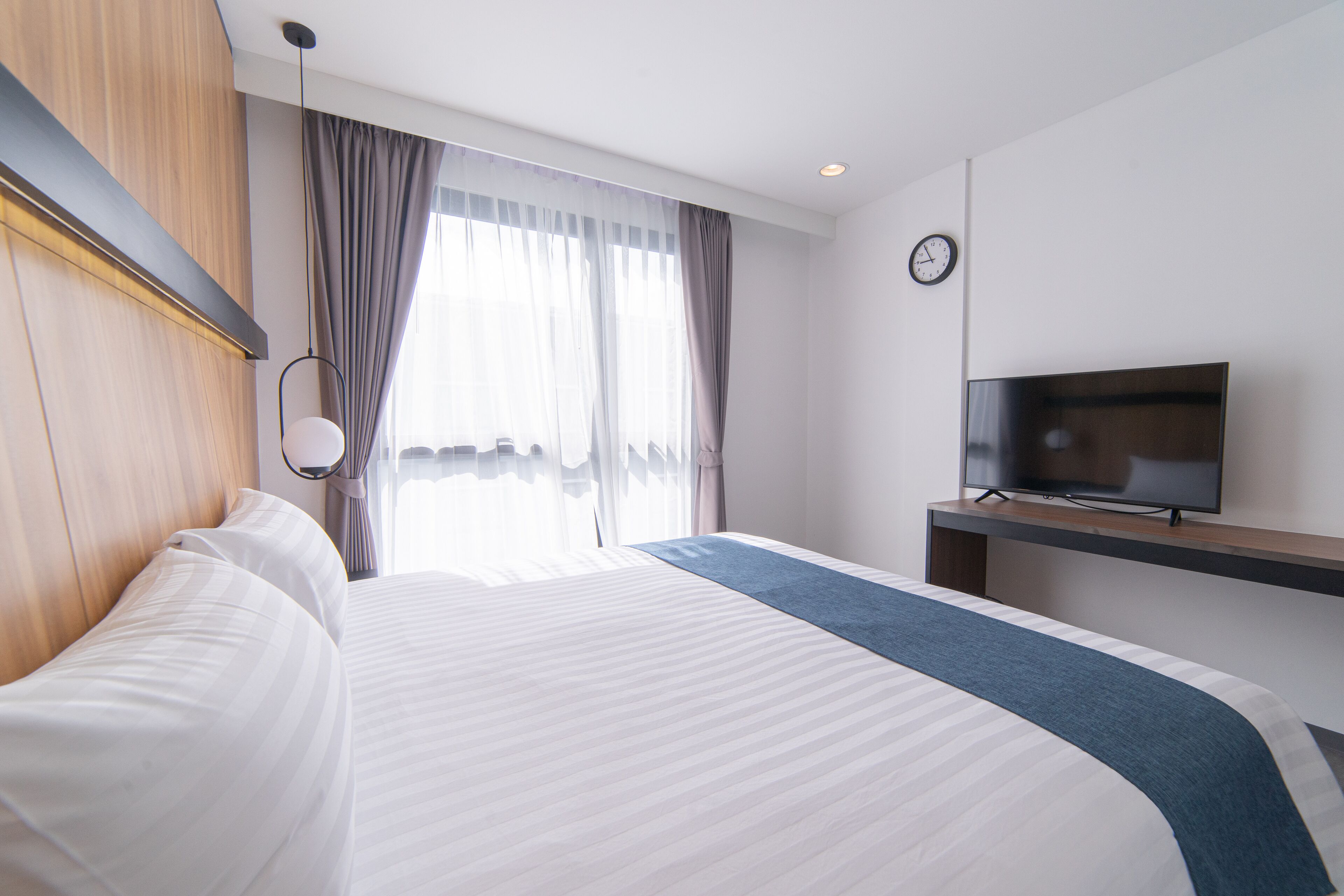 Ein Hotelzimmer mit einem großen Bett, einem Fernseher auf einem Schrank und einem Vorhangfenster.