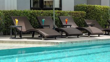 Una piscina con sillas de descanso y sombrillas, un flotador decorativo con forma de abeja y un edificio moderno al fondo.