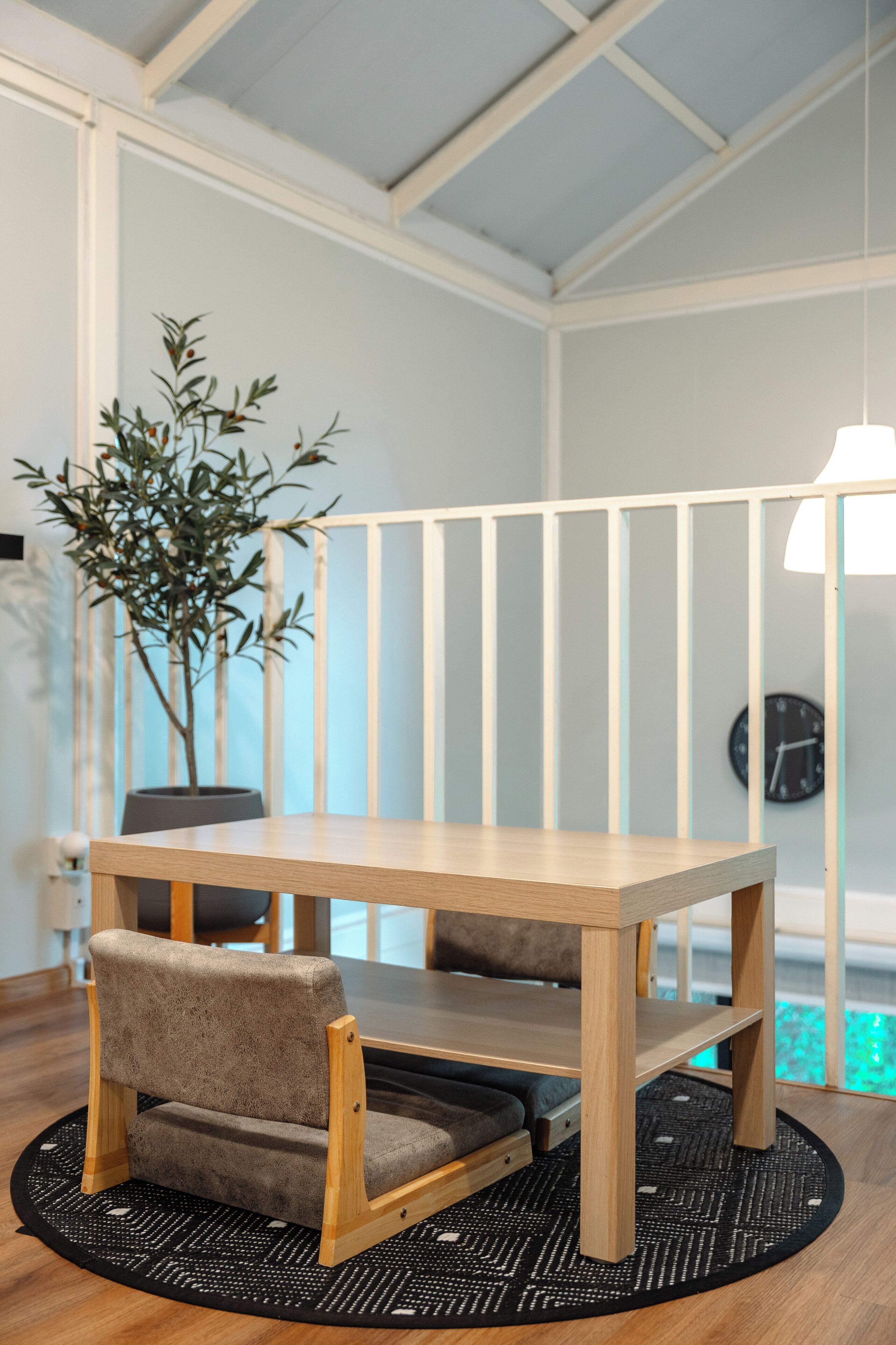 Una habitación con una mesa de madera, dos sillas, una planta en maceta, un reloj en la pared y una lámpara colgante.