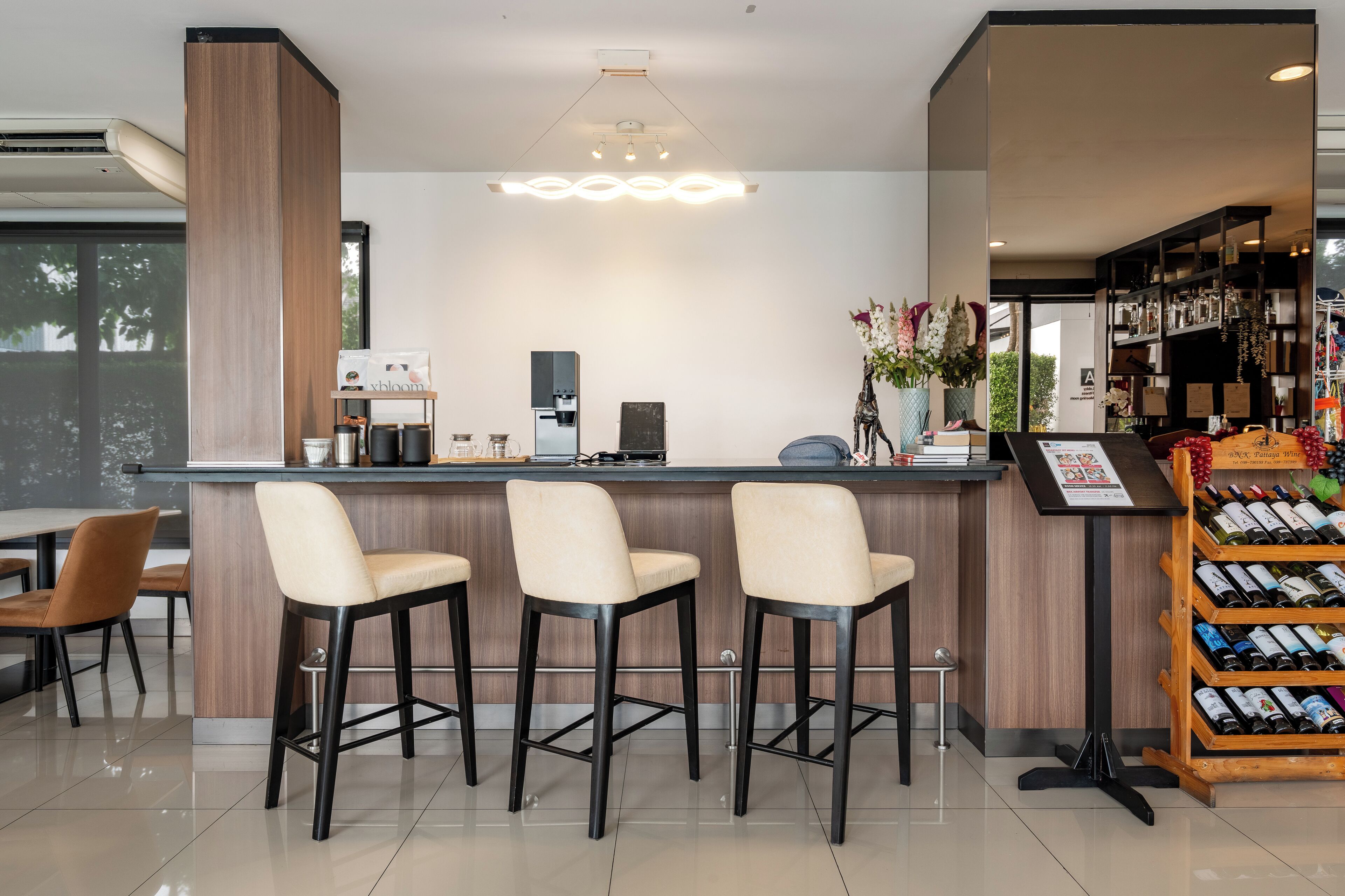 Un espace bar moderne comprenant un comptoir, trois tabourets de bar, une machine à café et un présentoir à bouteilles de vin.