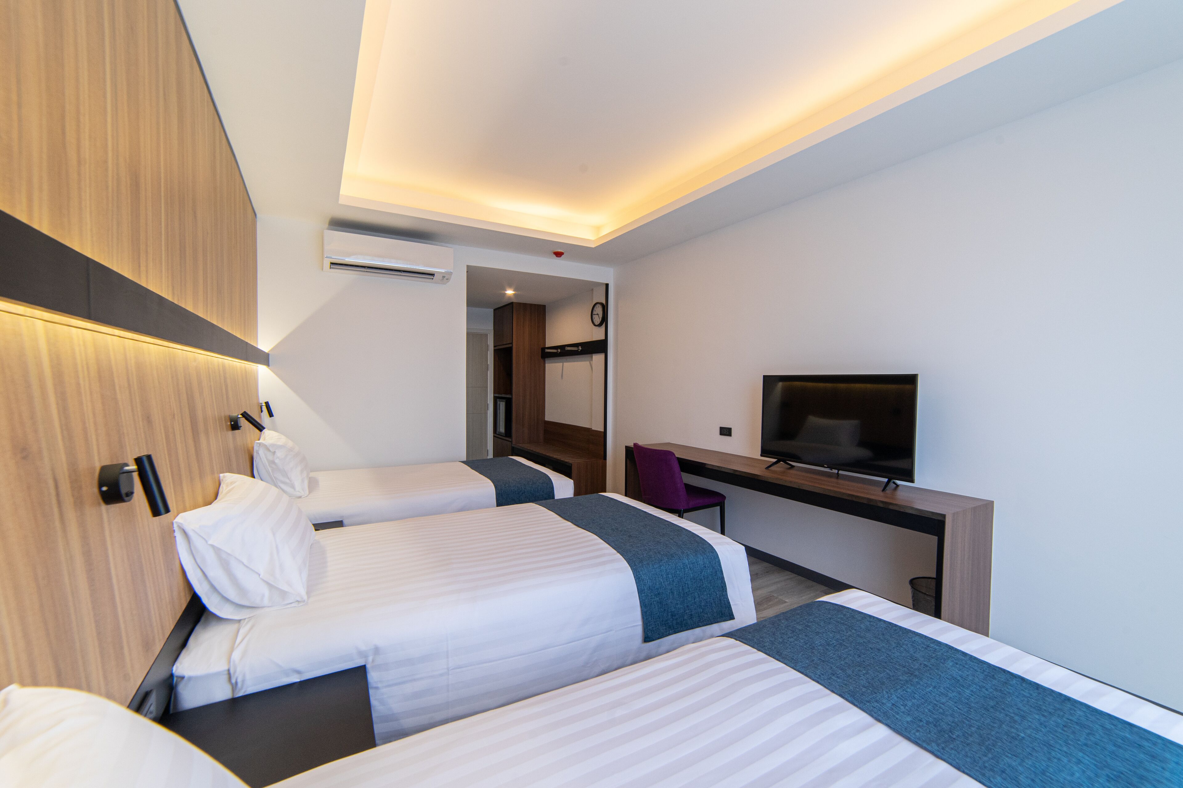 Quarto de hotel com duas camas, uma escrivaninha, uma cadeira, televisão e guarda-roupa.