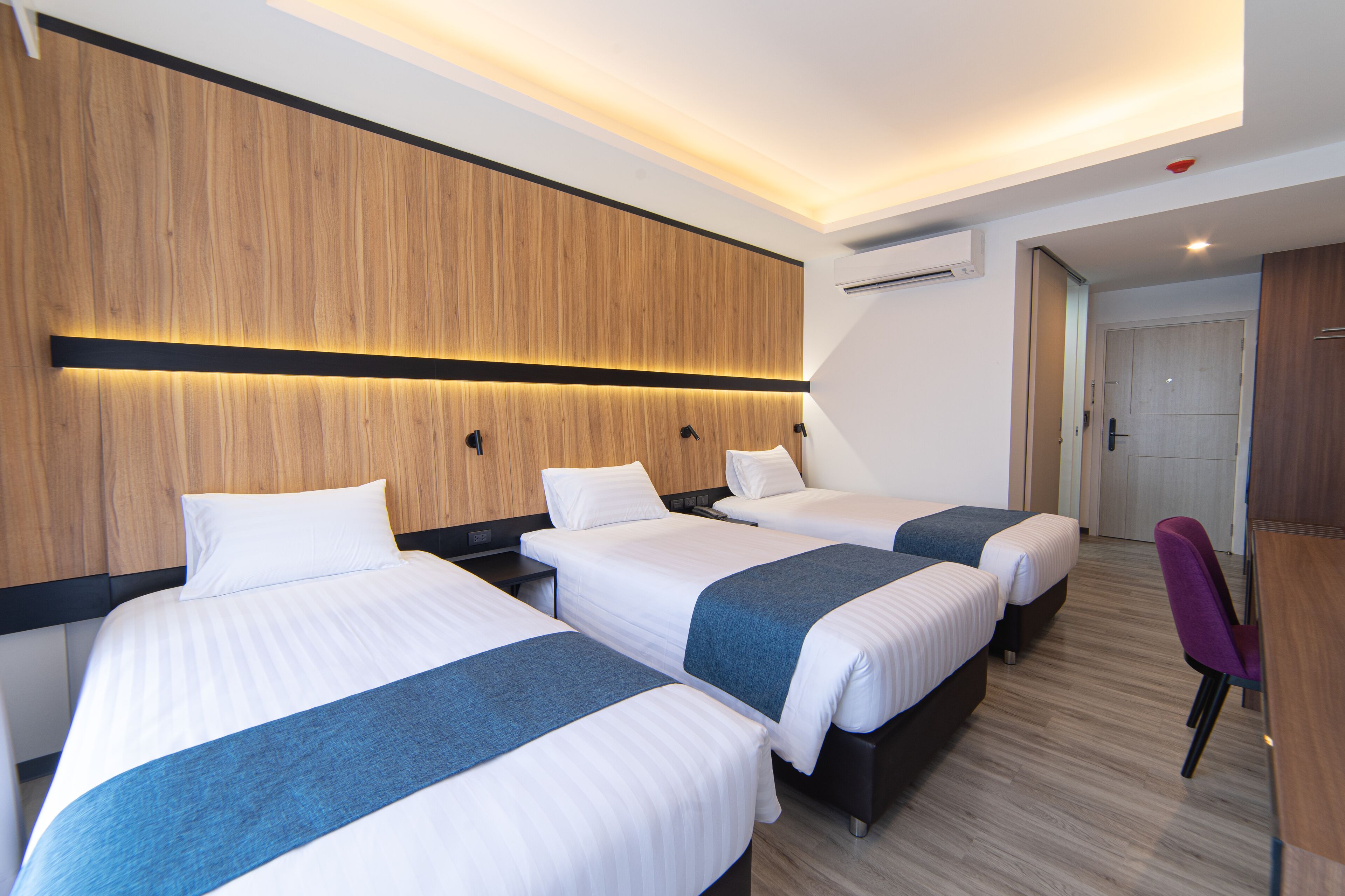 A hotel room with three beds, wooden paneling, and a modern design.