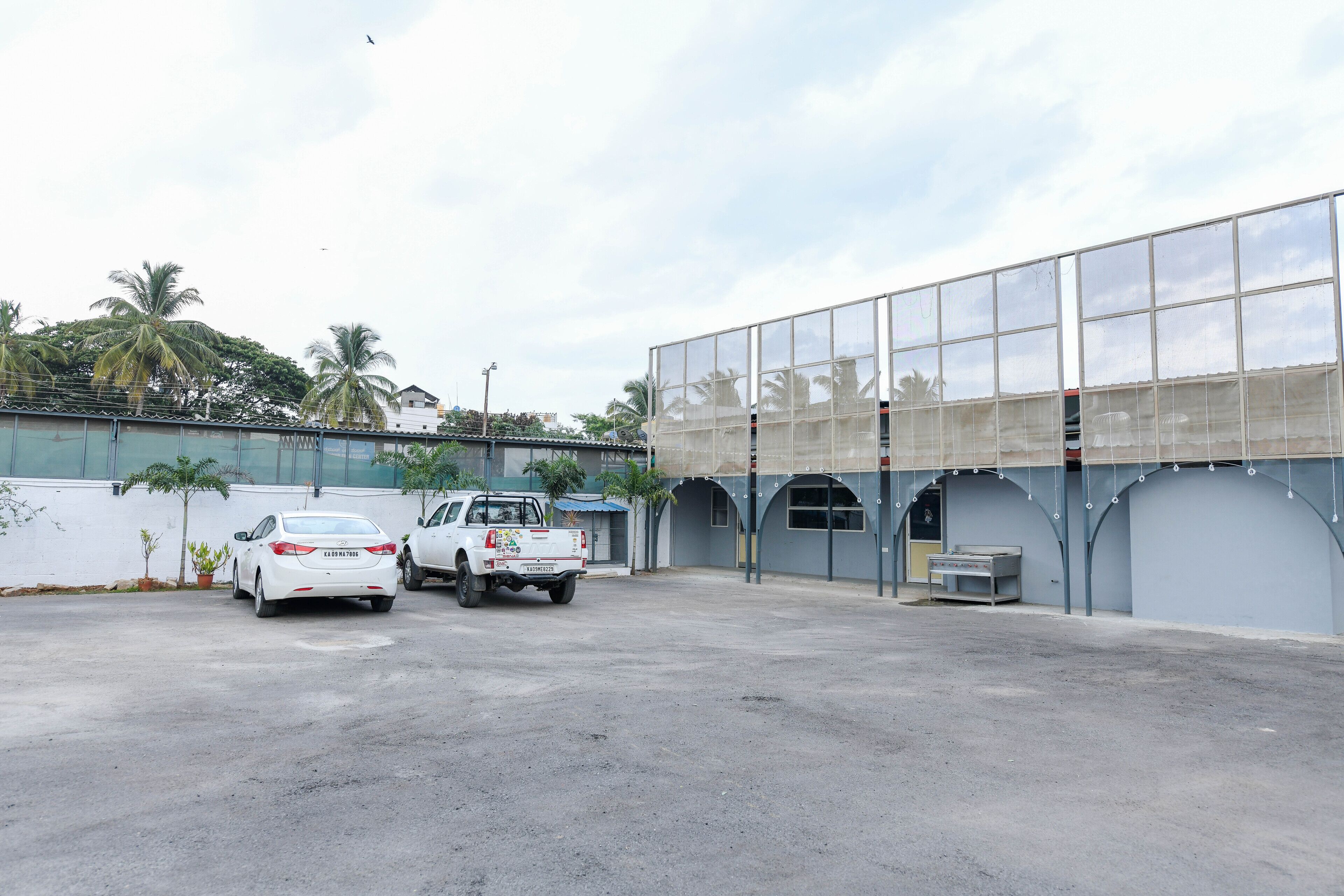 A parking area with a white car and a white pickup truck. There are palm trees and a building with a glass facade in the background.