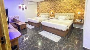 Quarto de hotel com duas camas, um sofá, uma escrivaninha e um papel de parede estampado.