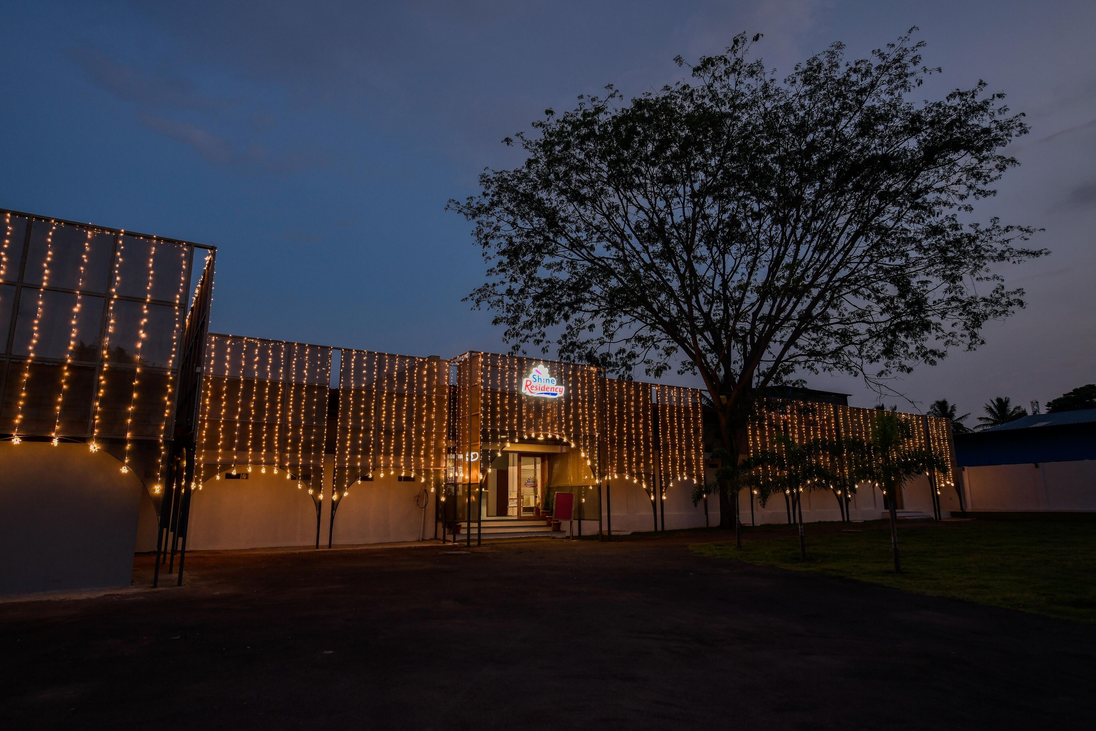 Un edificio con un letrero que dice "Shine Residency" y un árbol en la parte delantera.