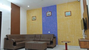 A living room with a brown sofa, a small round table, and a TV on a wooden cabinet. - Hotel Apni Haveli Villa (Udaipur)