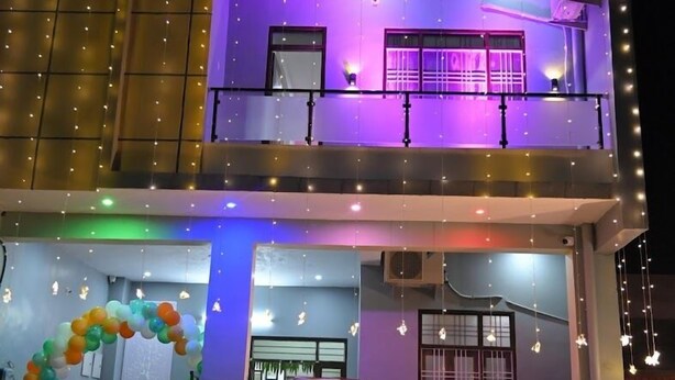 A two-story building with a sign reading "APNI Villa." It features a balcony with string lights and a sign, a reception area with chairs, and a sign indicating the villa's name and address. - Hotel Apni Haveli Villa (Udaipur)