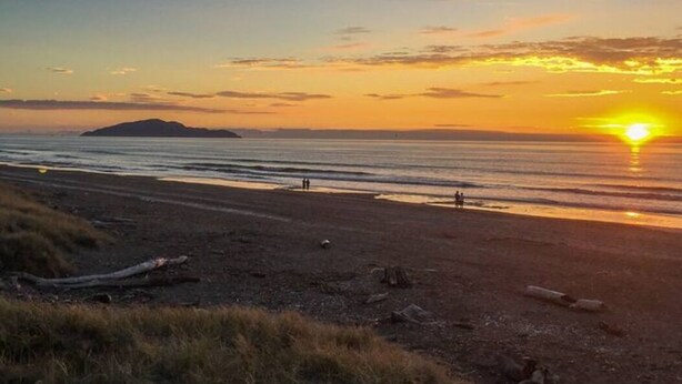 Une plage au coucher du soleil, avec une eau calme et une île qui se dessine à l'horizon.