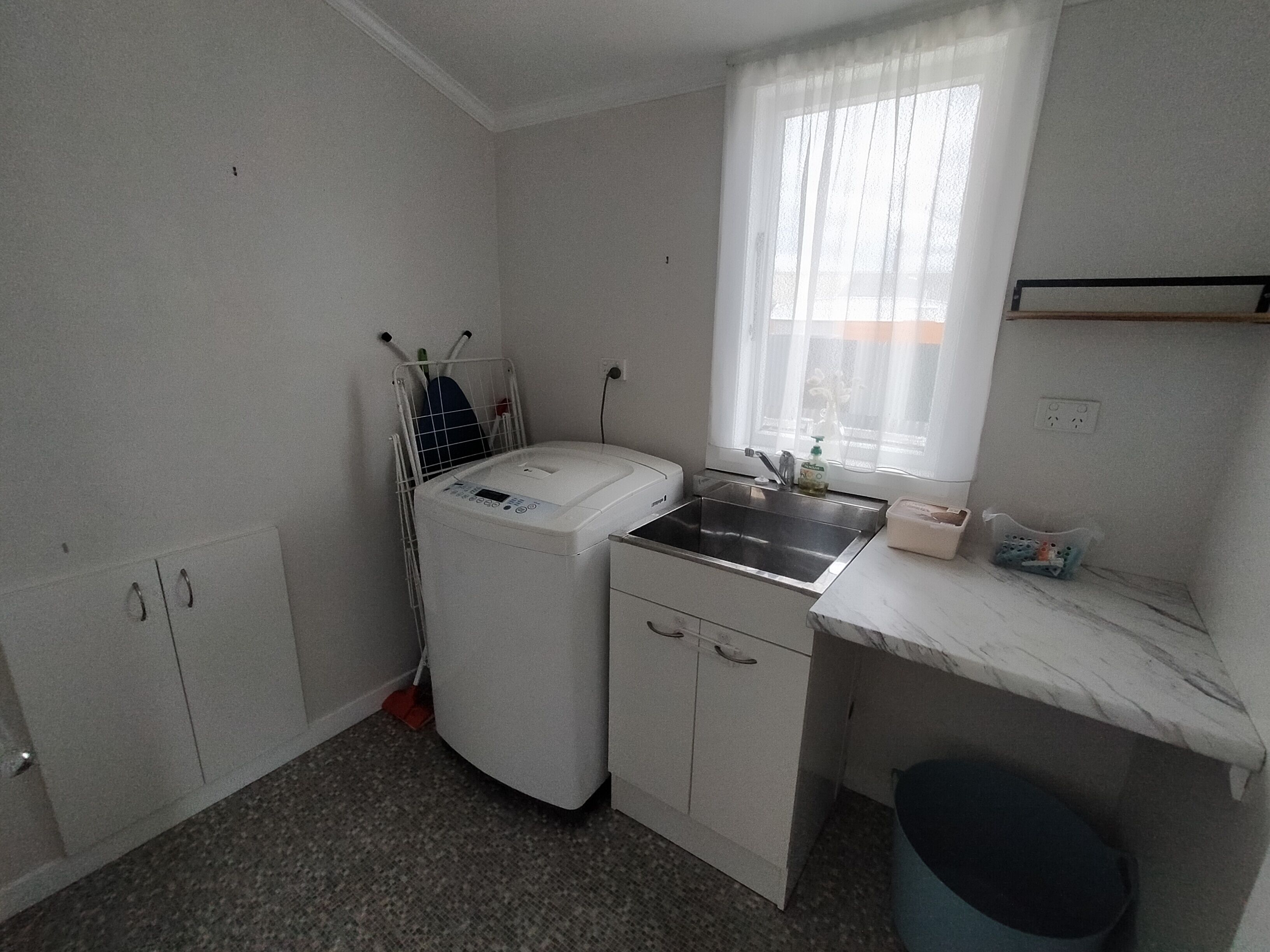 Kompakti pyykinhuoltotila, jossa on pesukone, kuivausrumpu, pesuallas ja pieni roskakori.