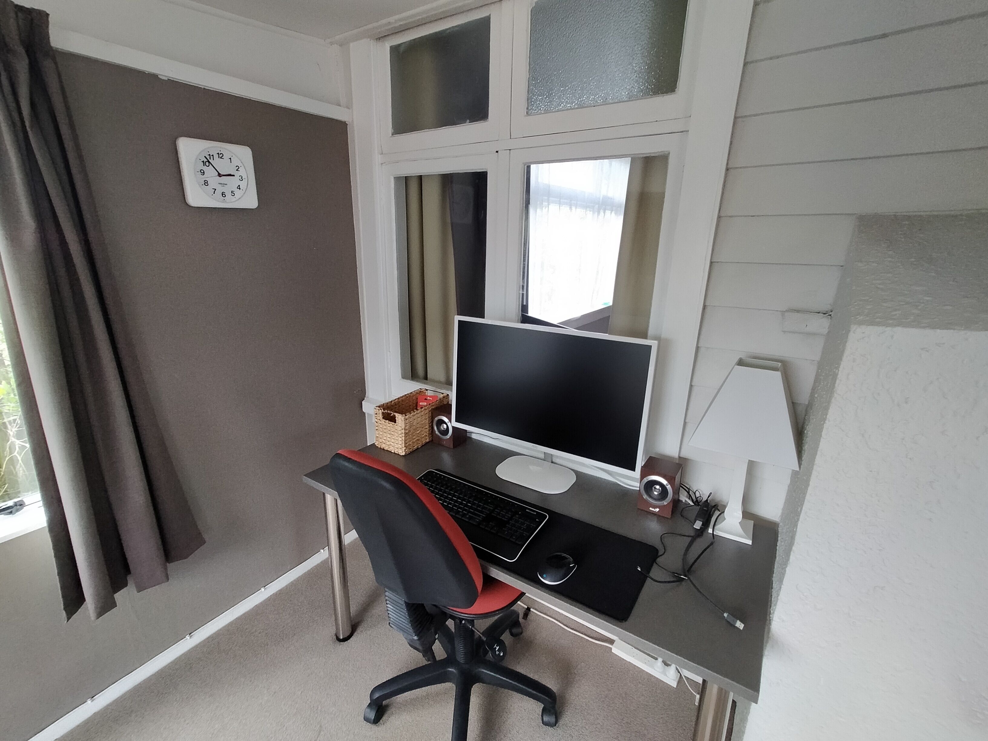Una postazione da lavoro a casa con scrivania, computer, sedia e finestra con tende.