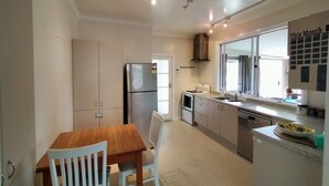 Une cuisine compacte comprenant une table à manger, des placards blancs, un réfrigérateur, une cuisinière et une fenêtre donnant sur un paysage agréable.
