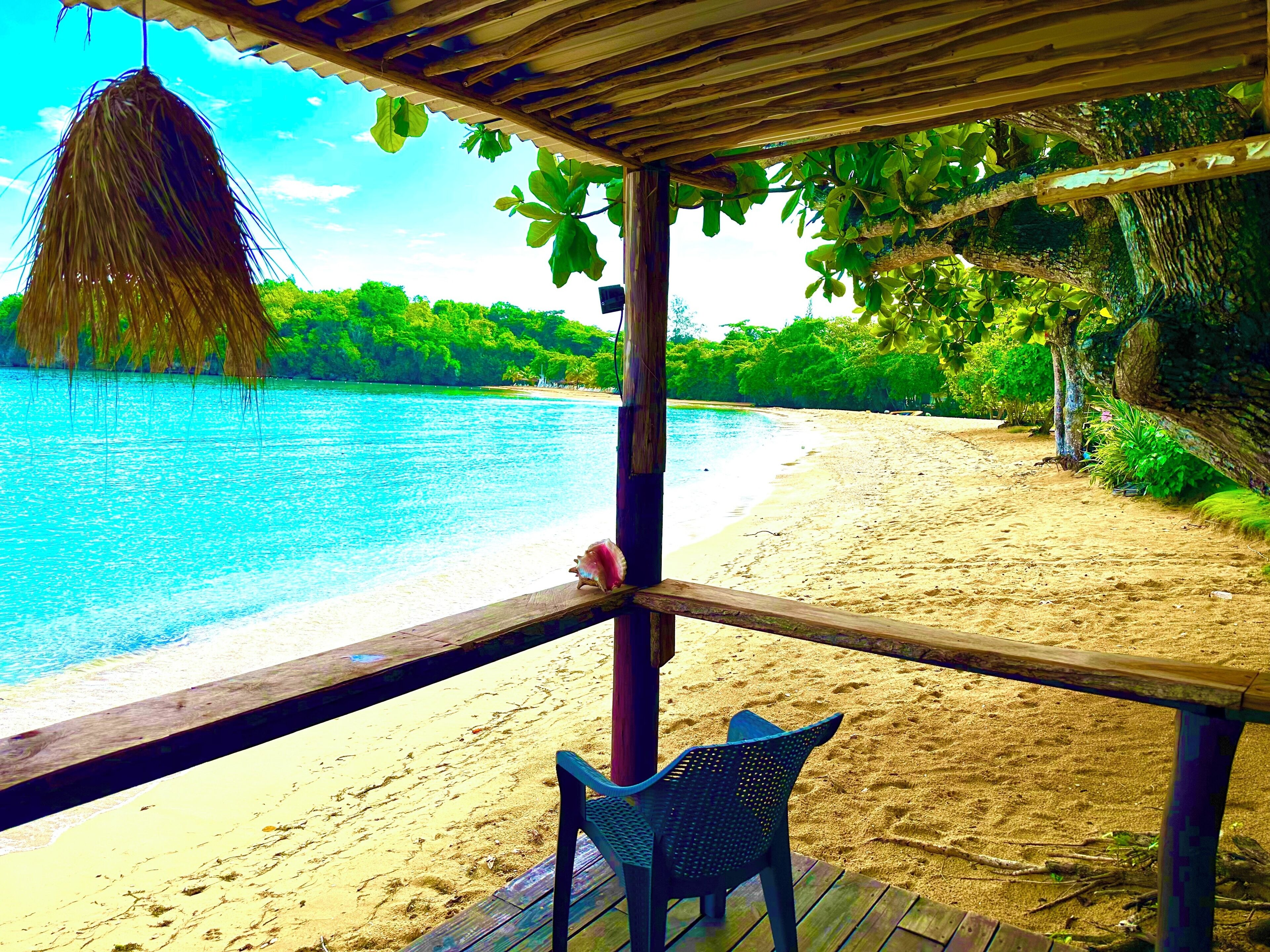 Une vue sur la plage depuis une terrasse en bois, avec une chaise et un auvent en chaume.