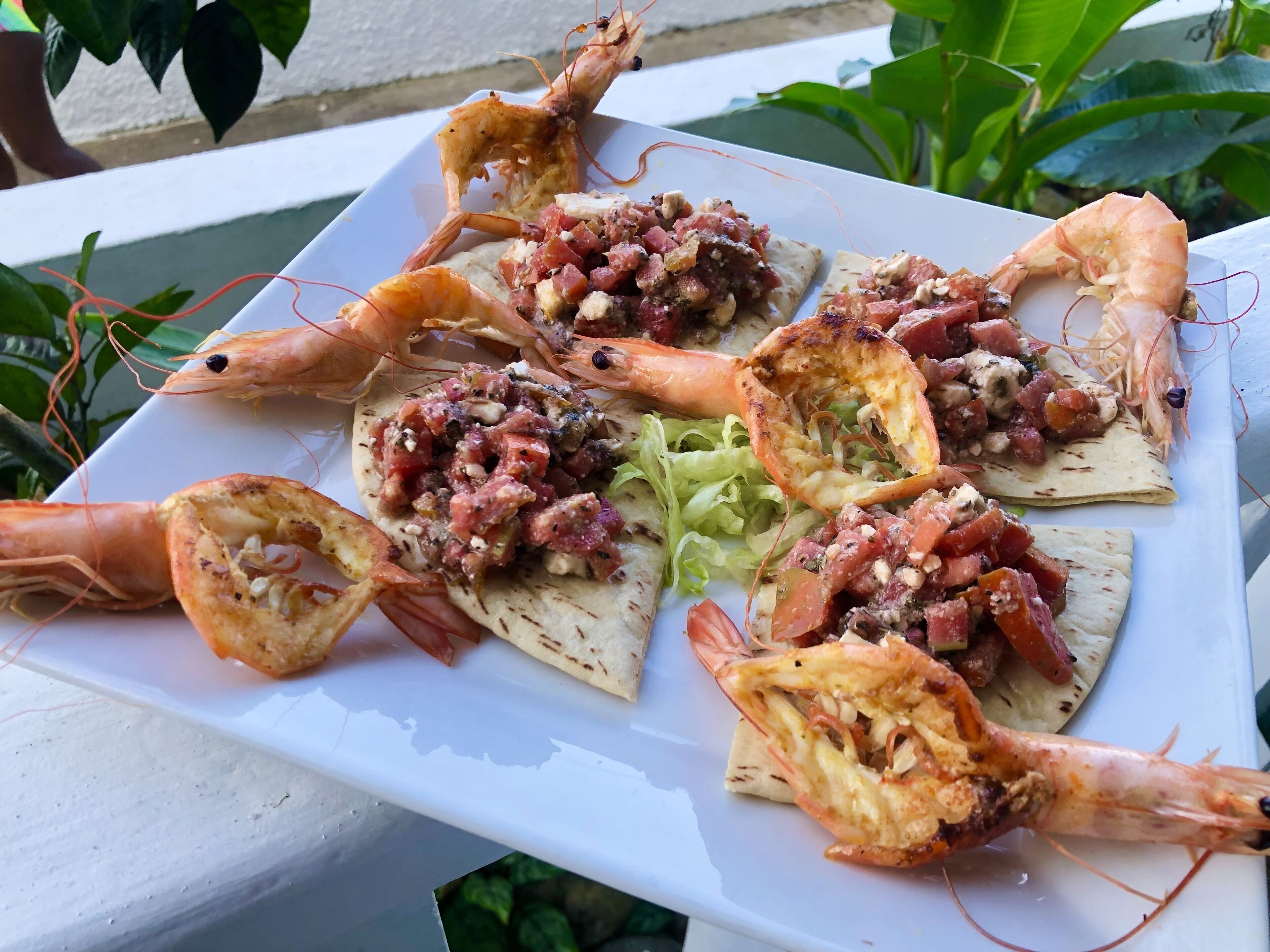 Un plato blanco con camarones a la parrilla y pan plano cubierto con salsa de tomate y nueces.